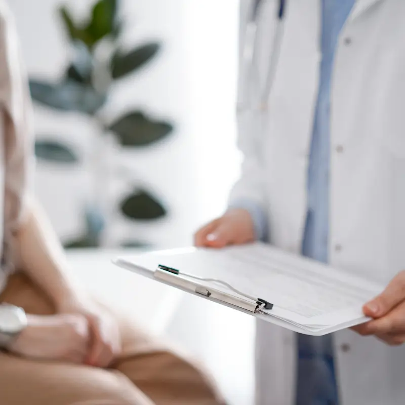 Allied health professional holding a clipboard during an informed consent discussion with a seated patient