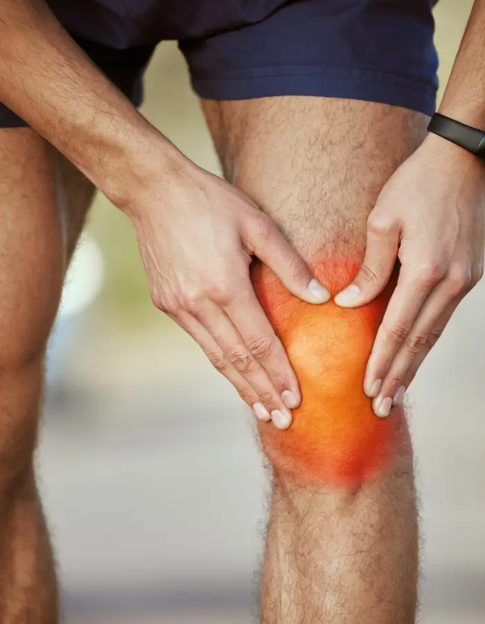 Man holding his knee in pain with a red-highlighted area, indicating knee injury or inflammation