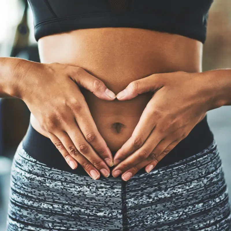 Close-up of a woman's hands forming a heart shape over her stomach, representing the positive impact of probiotics on gut health