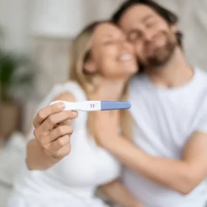 Happy couple holding a positive pregnancy test during a fertility journey.