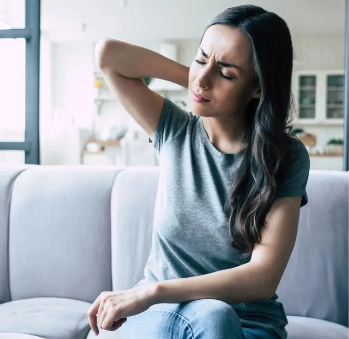 Young woman experiencing neck pain due to poor posture while sitting on a couch